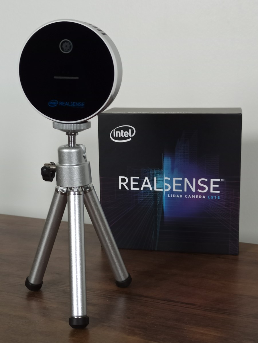 작은 삼각대에 세운 원형의 검은색 RealSense 카메라와 뒤쪽의 제품 상자.